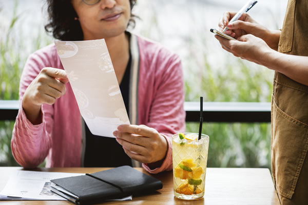 Waiter sedang mencatat pesanan tamu secara manual menggunakan kertas